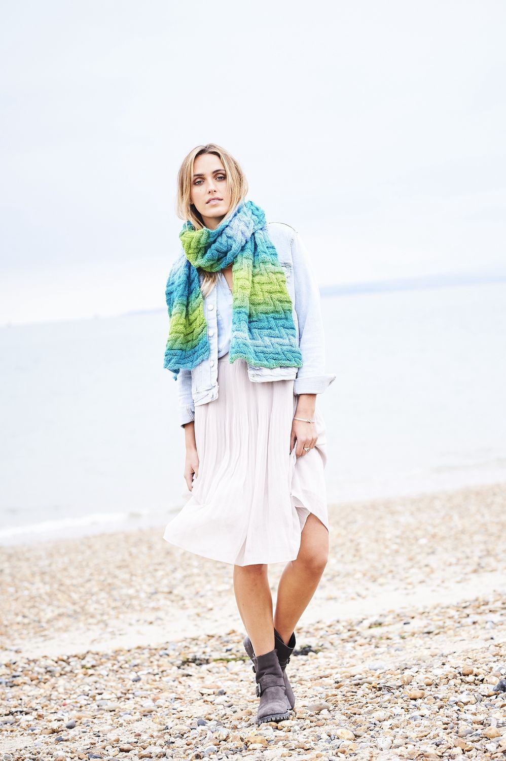 A woman is wearing a knitted scarf in a variegated blue and green yarn.