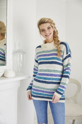 A woman is wearing a cream knitted sweater with silver, green, purple, teal and navy blue stripes.