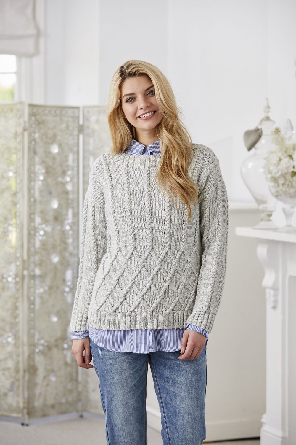 A woman is wearing a pale grey cable knit sweater.