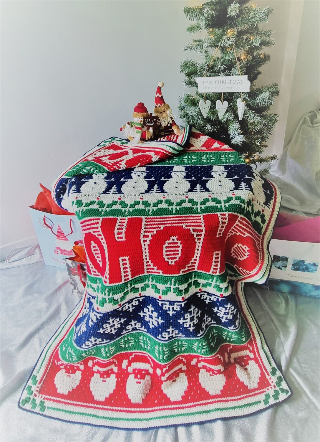 The festive design crocheted blanket in shades of cream, red, green and navy blue.