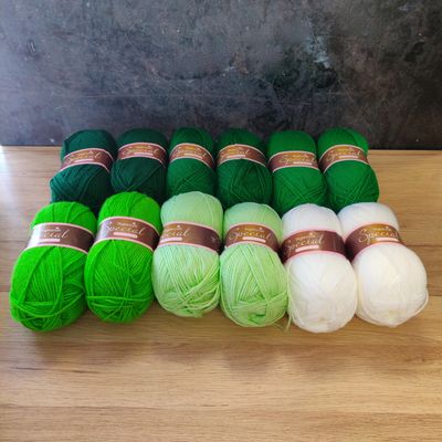 12 balls of yarn in shades of green and white laid out on a wooden surface.