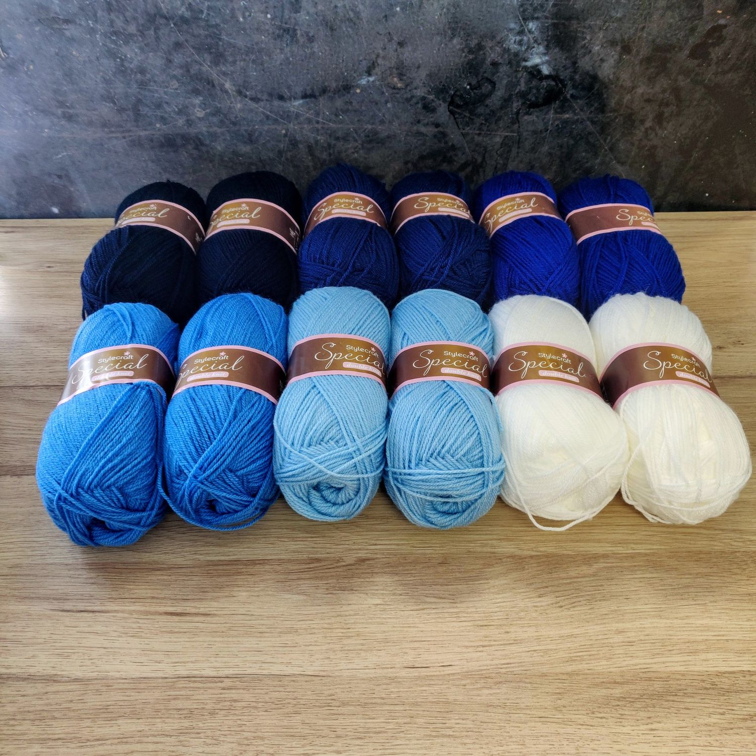 12 balls of yarn in shades of navy, blue and white laid out on a wooden surface.