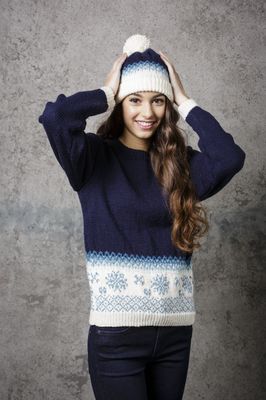 A woman is wearing a navy blue knitted sweater with white and light blue colourwork snowflakes and a matching hat.