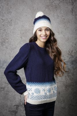A woman is wearing a navy blue knitted sweater with white and light blue colourwork snowflakes and a matching hat.