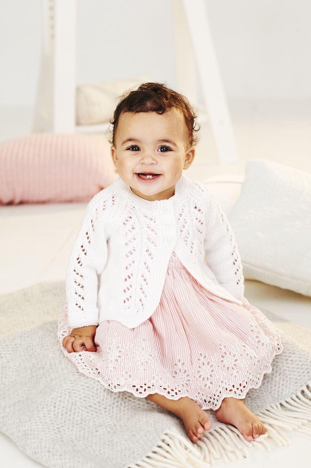 A baby is wearing a white lacy knitted cardigan.