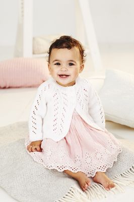 A baby is wearing a white lacy knitted cardigan.