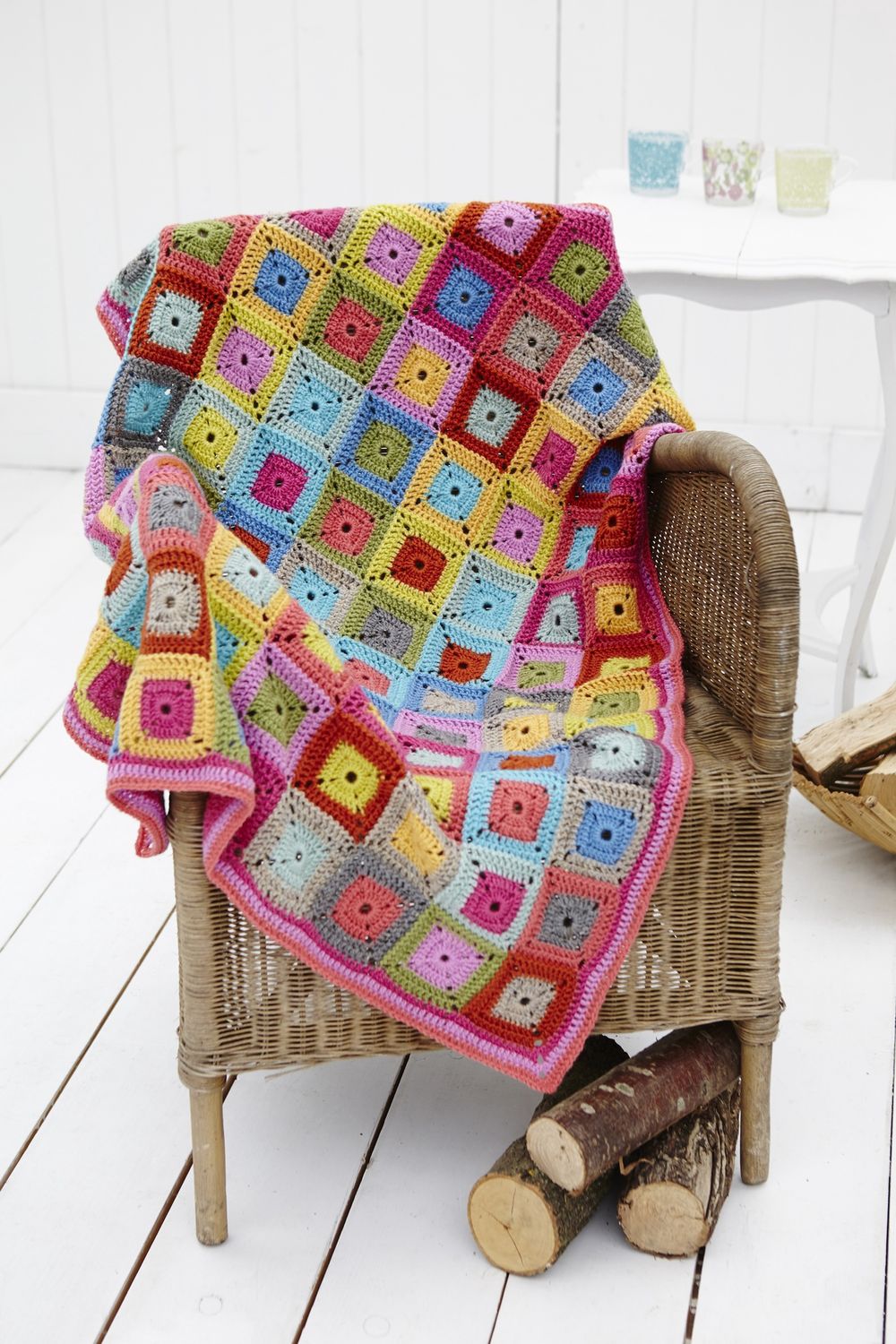 A crocheted blanket made up of blue, green, pink, purple, orange and yellow squares.