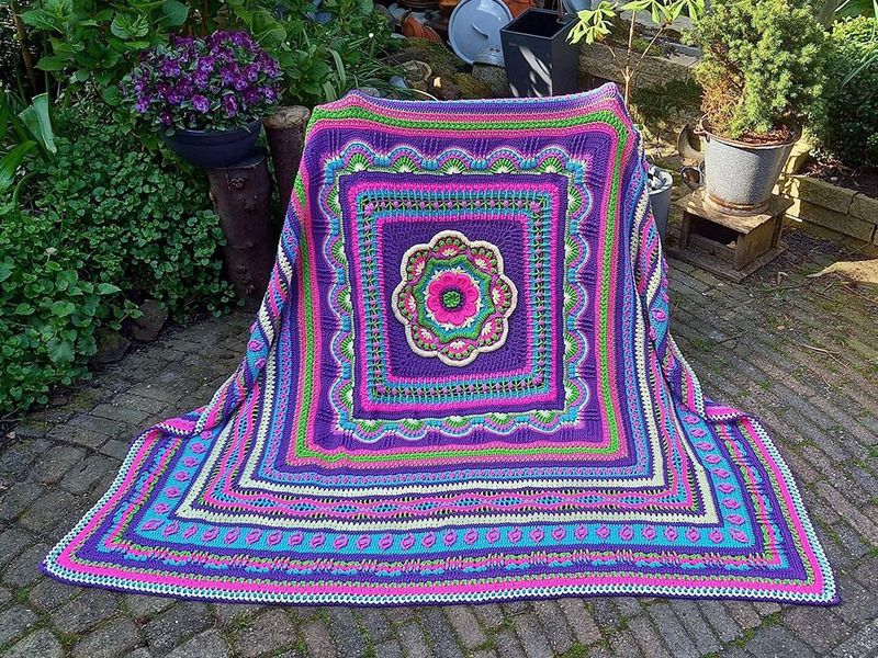 A crocheted blanket in pink, purple, blue and green.