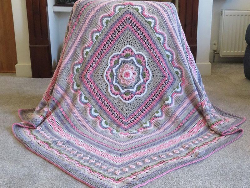 A crocheted blanket in pink, grey, purple and white.