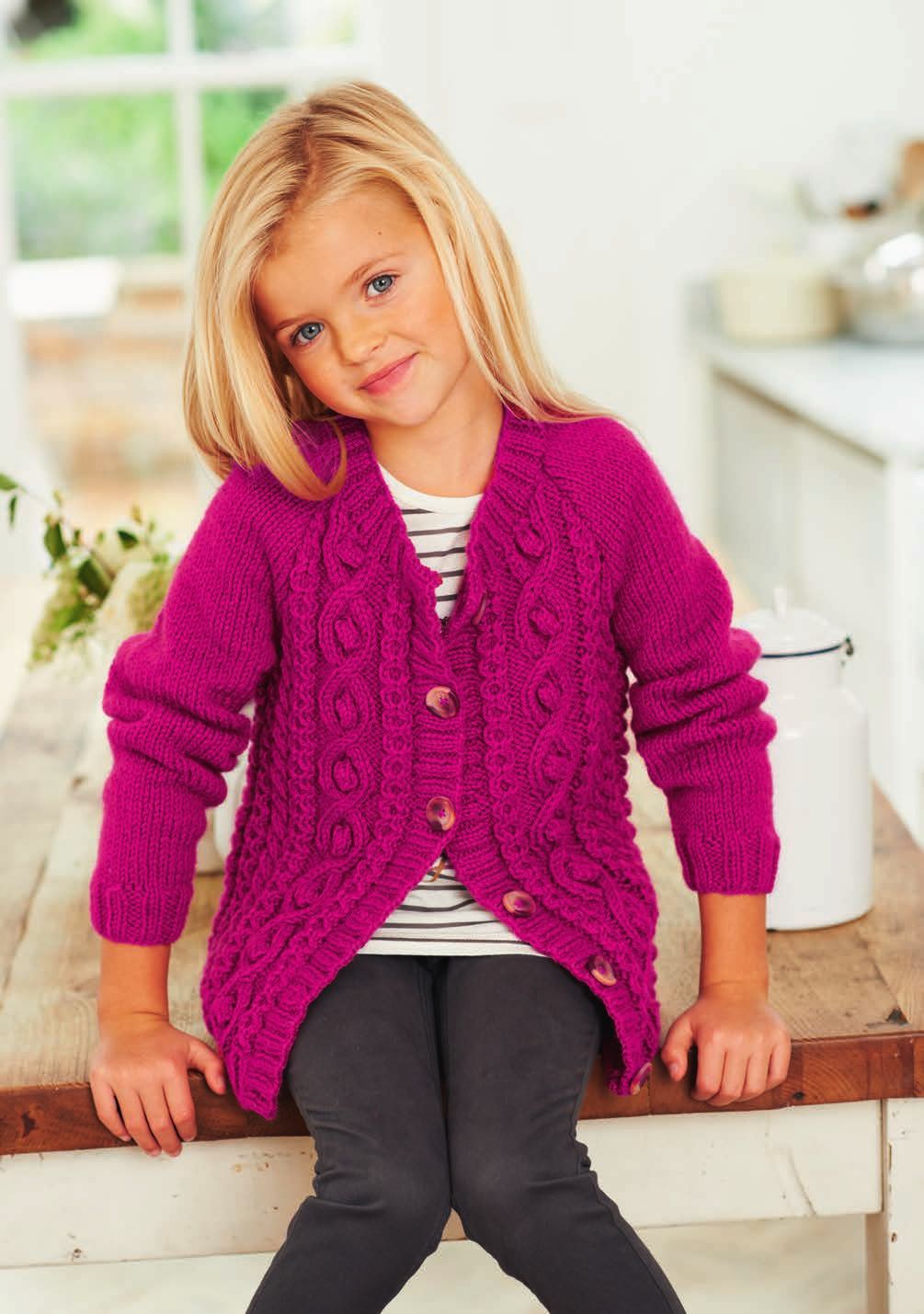 A girl is wearing a bright pink cable knit cardigan.