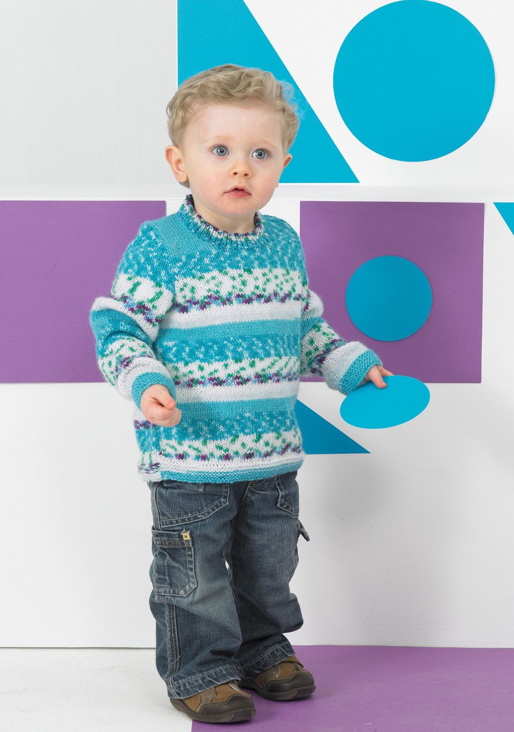 A boy is wearing a knitted sweater in a variegated blue yarn.