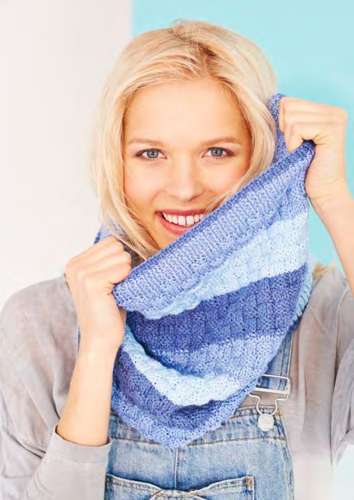 A woman is wearing a knitted cowl in a variegated blue yarn.