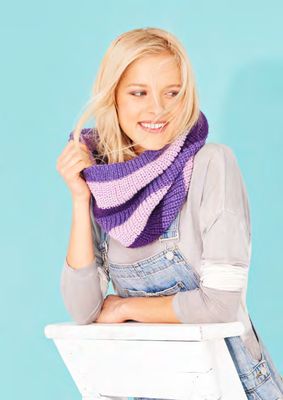 A woman is wearing a knitted cowl in a variegated purple yarn.