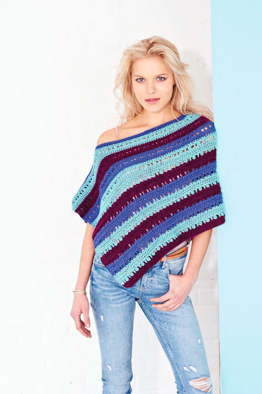 A woman is wearing a crocheted poncho in a variegated blue and burgundy yarn.
