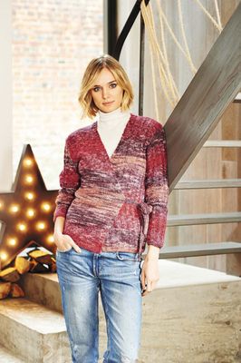 A woman is wearing a knitted cardigan in a variegated red yarn.