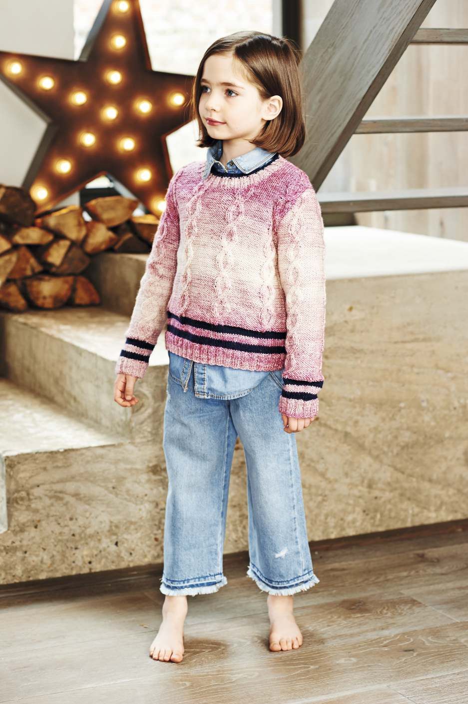 A girl is wearing a knitted sweater in a variegated pink yarn with navy stripes on the bottom edge.