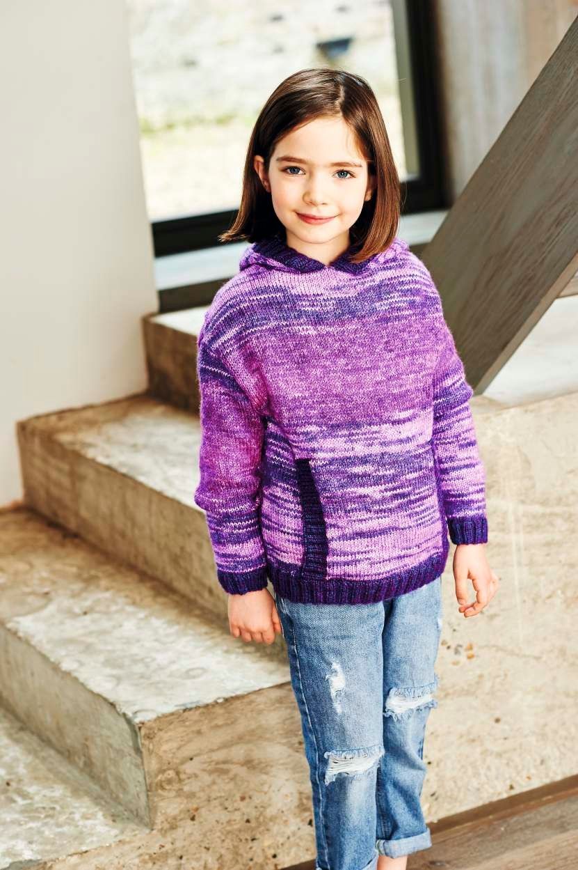 A girl is wearing a knitted sweater in a variegated purple yarn.