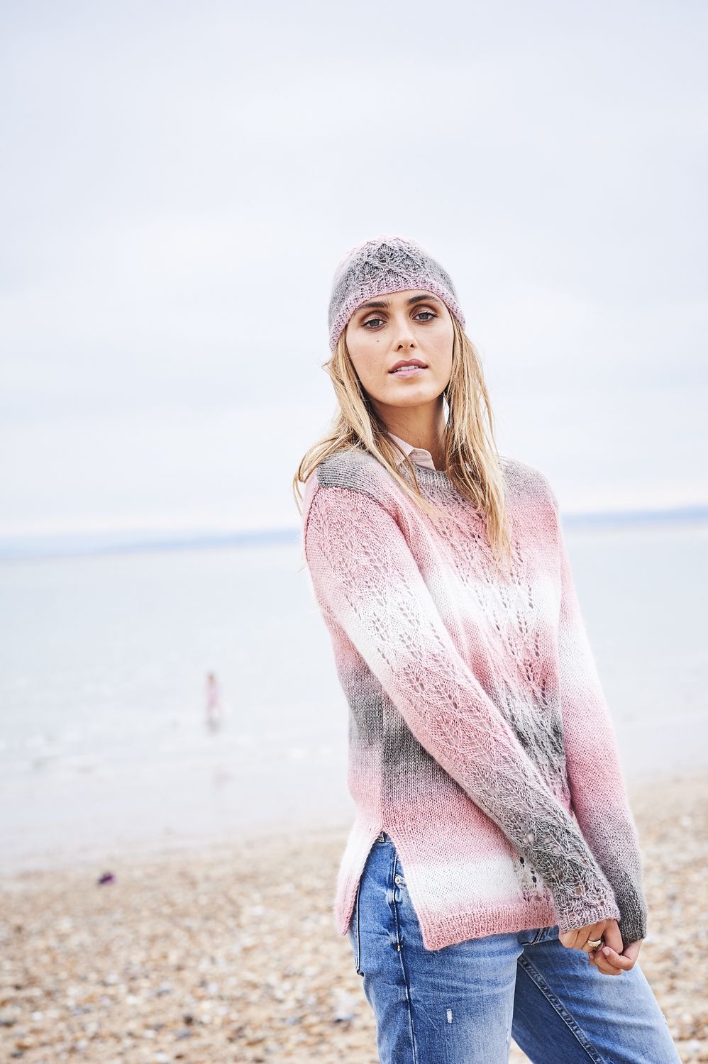 A woman is wearing a knitted sweater and matching hat in a variegated pink and grey yarn.