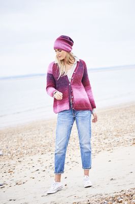 A woman is wearing a knitted cardigan and matching hat in a variegated pink yarn.