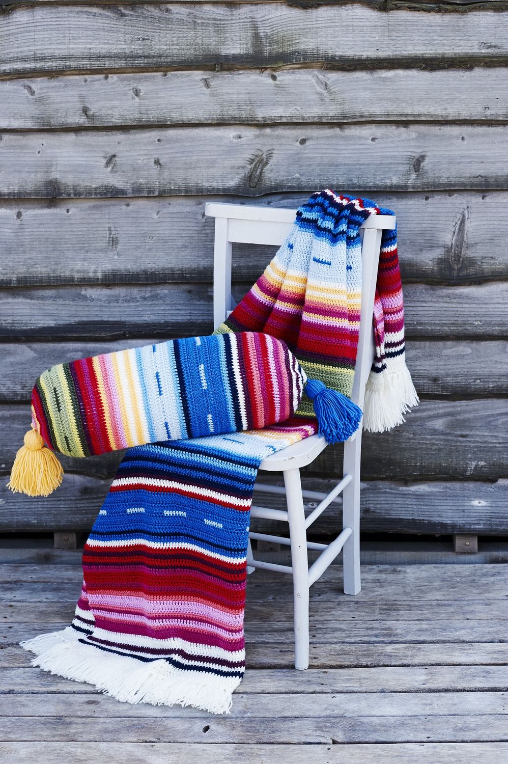A stripy crocheted blanket and matching cushion in shades of blue, red, yellow, green and purple.