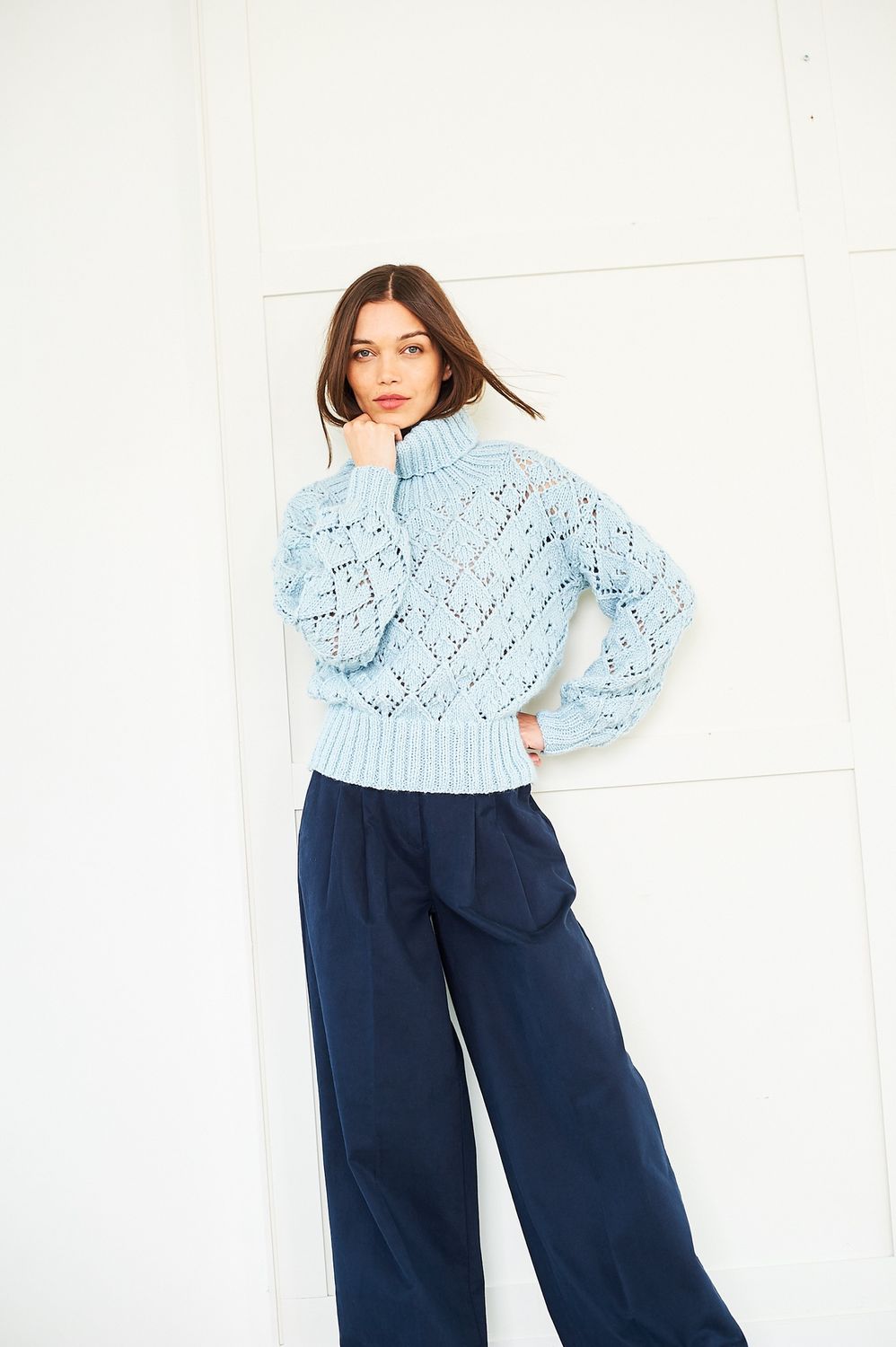 A woman is wearing a light blue knitted sweater with a diamond lace pattern.