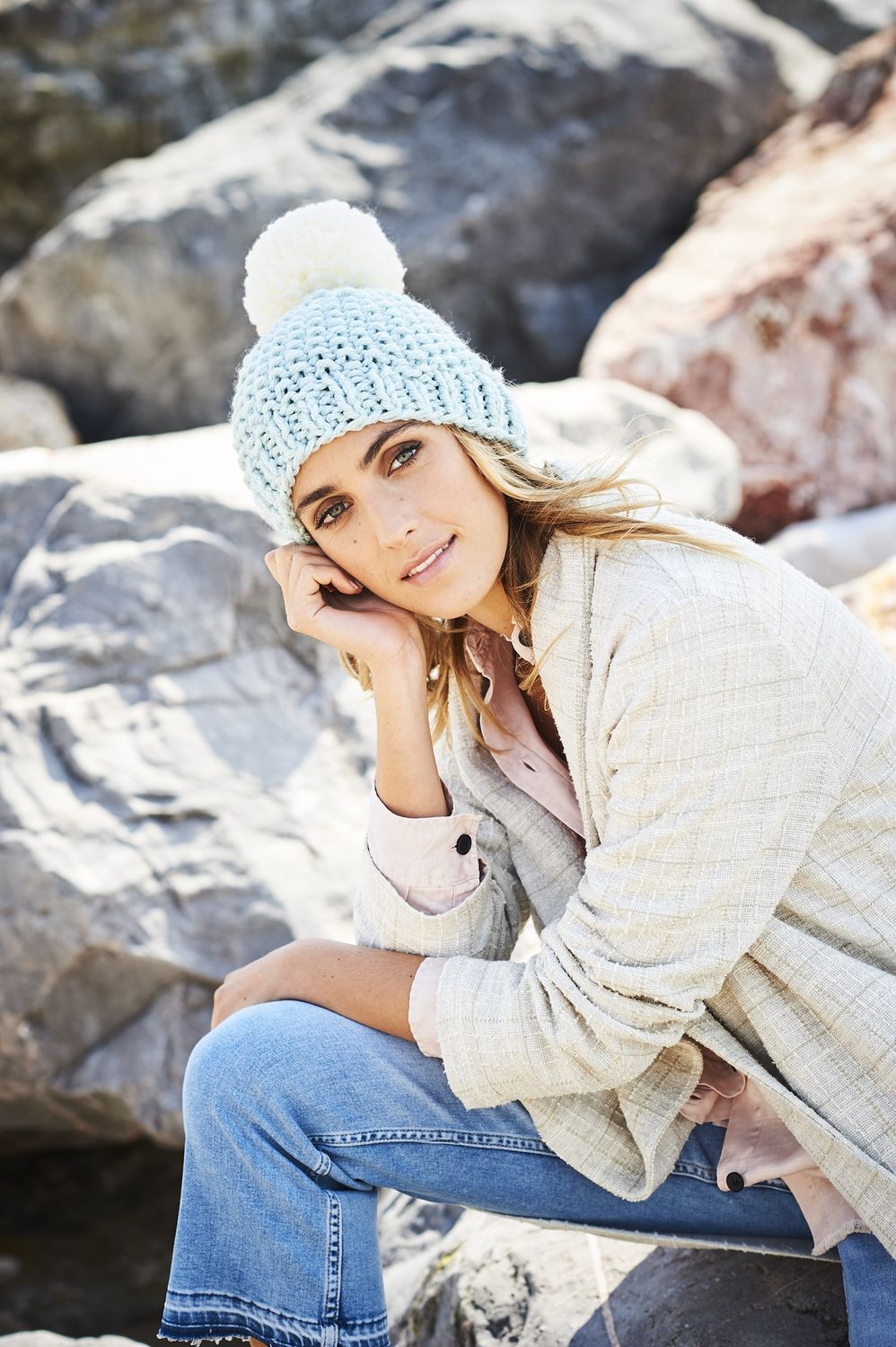 A woman is wearing a light blue knitted hat with a white pompom.