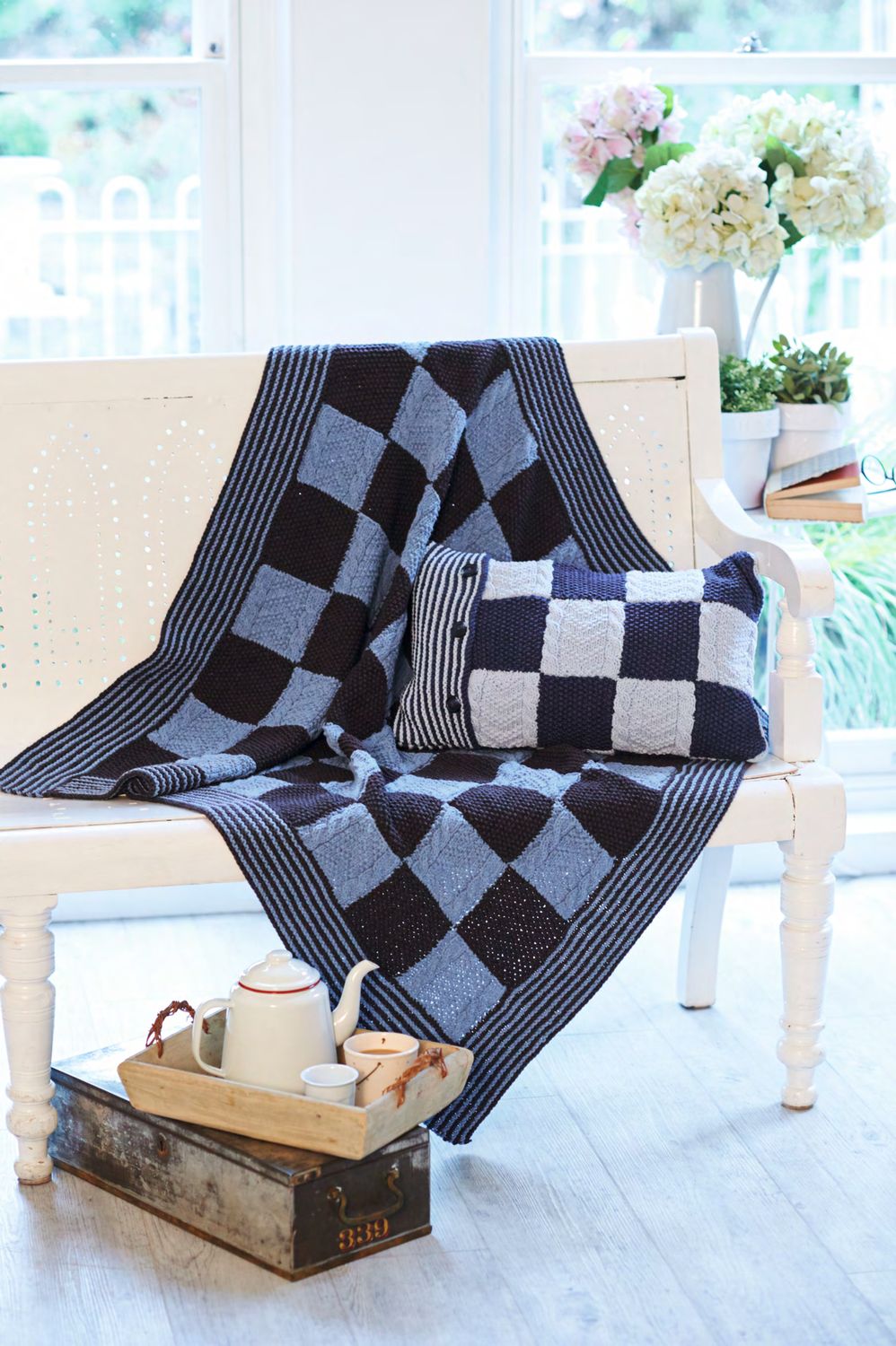 A knitted blanket and matching cushion in light and dark blue squares.