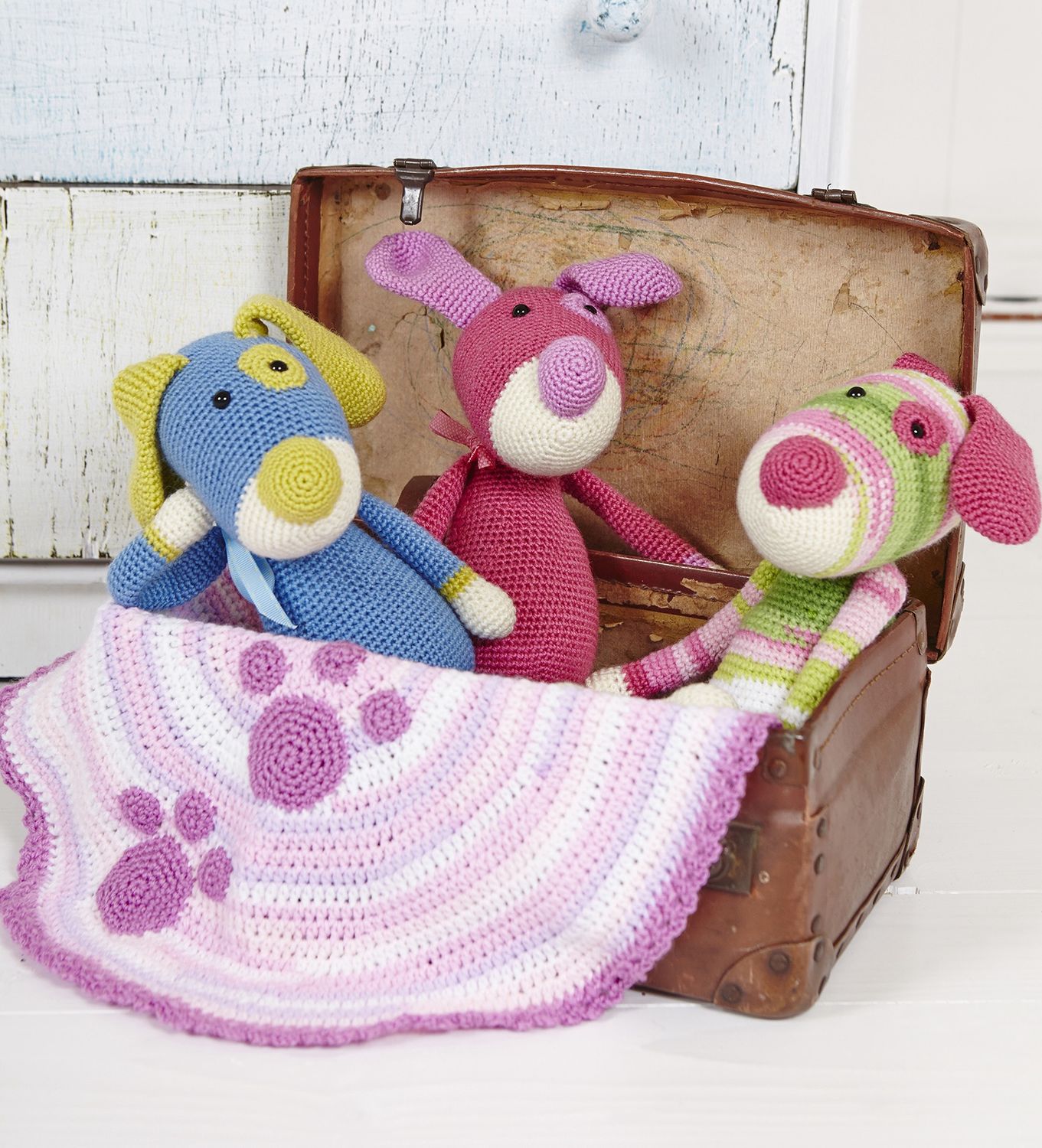 3 crocheted dogs in blue, pink and variegated green and pink alongside a small stripy pink crocheted blanket.