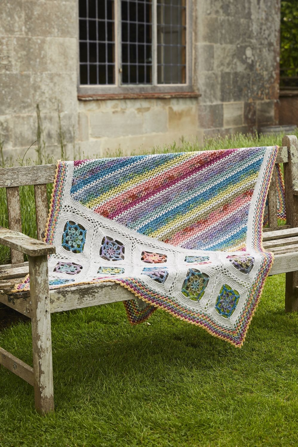 A crocheted blanket with multicoloured stripes and silver squares with colourful centres joined to one end.
