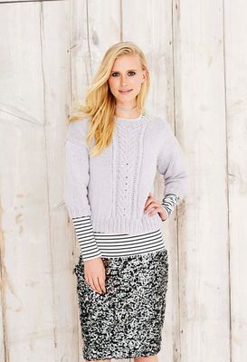 A woman is wearing a light grey knitted sweater with cable down the front centre.