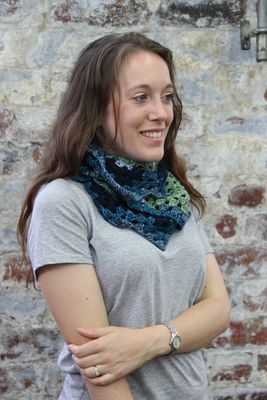 A woman is wearing a crocheted cowl in a variegated blue and green yarn.