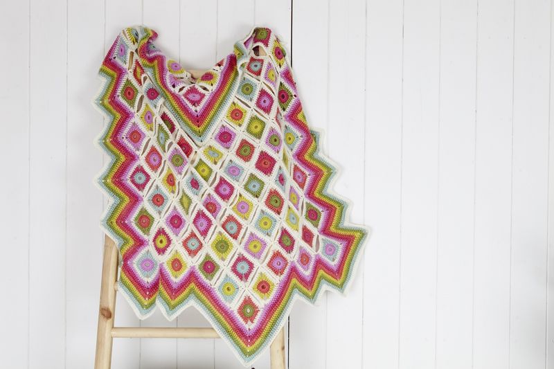 A crocheted blanket made up of cream, pink, green and blue squares.