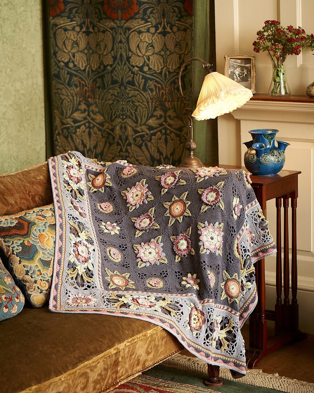A grey crocheted blanket with colourful 3D flower motifs.