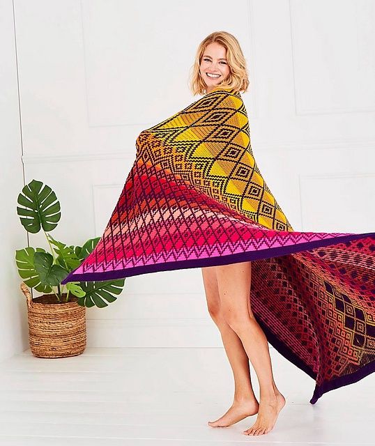 A woman has the large version of this blanket in reds, yellows, pinks and purple draped around her shoulders.