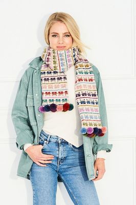 A woman is wearing a cream knitted scarf with pink, purple, red, green and blue colourwork houses.