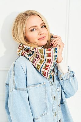 A woman is wearing a cream knitted cowl with pink, red, green and blue colourwork houses.