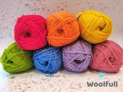 7 balls of yarn in rainbow shades piled up.