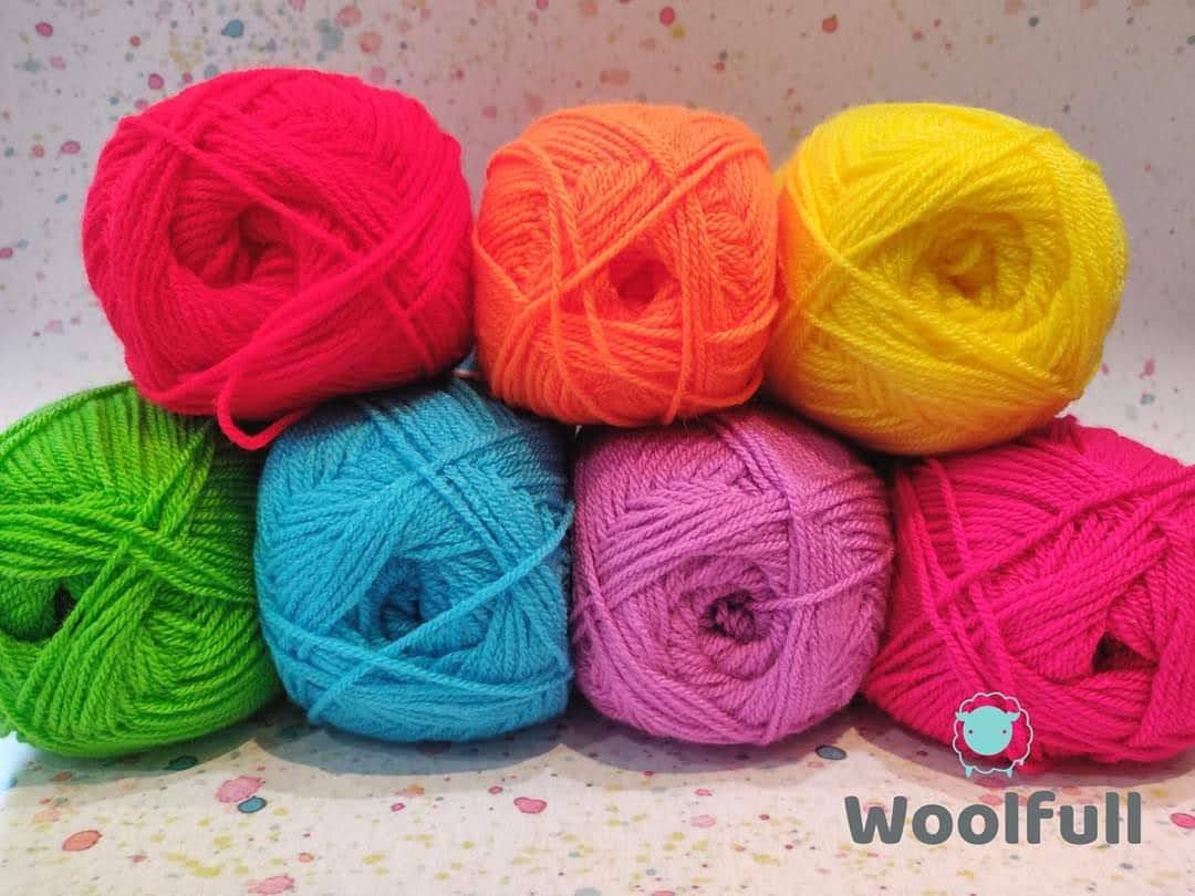 7 balls of yarn in bright rainbow shades piled up.