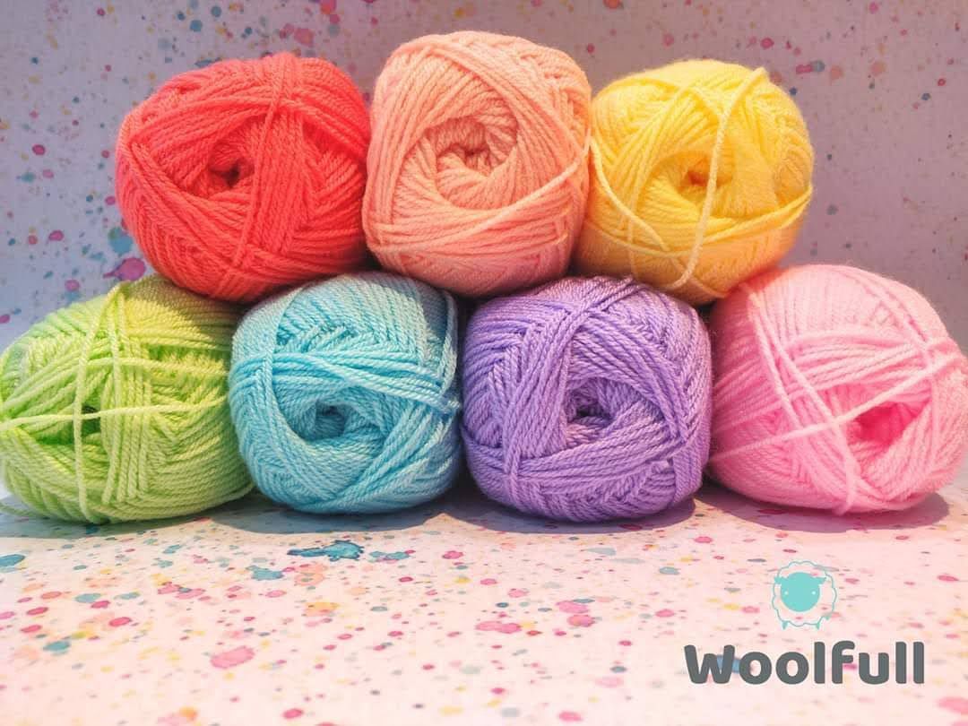 7 balls of yarn in pastel rainbow shades piled up.