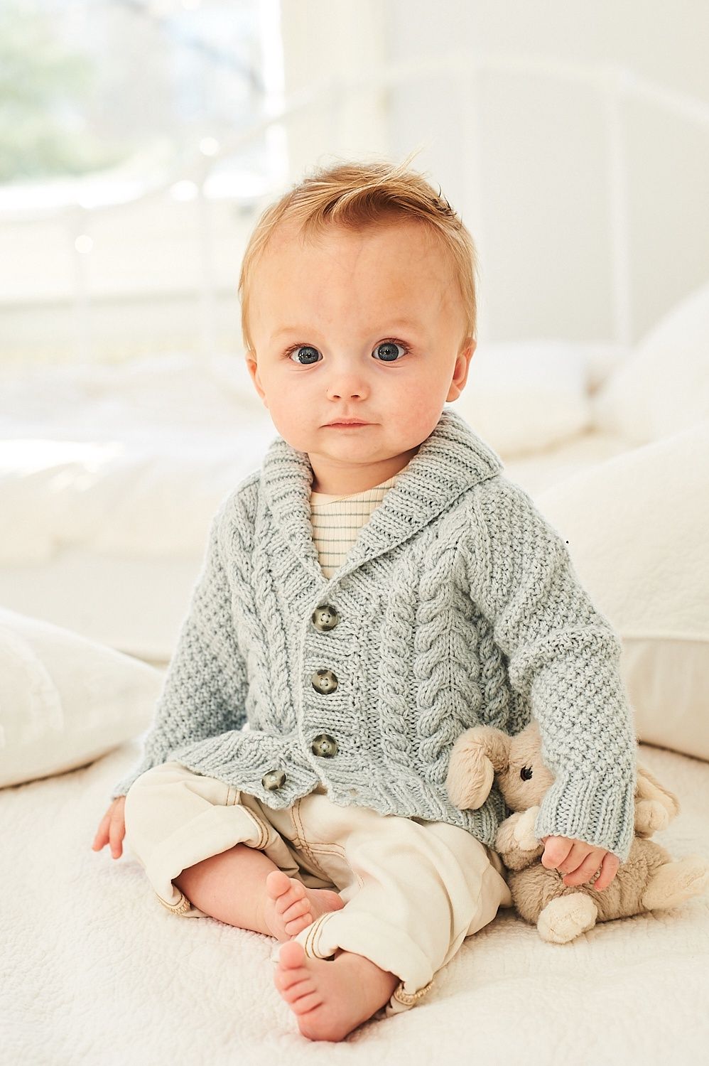 A baby is wearing a light grey cable knit cardigan.
