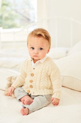 A baby is wearing a cream cable knit cardigan.