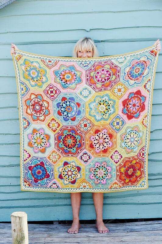 A woman is holding a crocheted blanket made up of octagons and squares in shades of yellow, blue, purple, red, green, pink and orange.