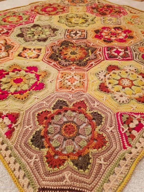 A close up of a crocheted blanket made up of octagons and squares in shades of brown, green, red and mustard.