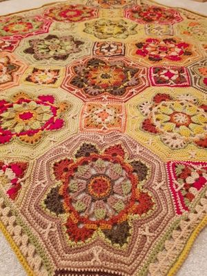 A close up of a crocheted blanket made up of octagons and squares in shades of brown, green, red and mustard.