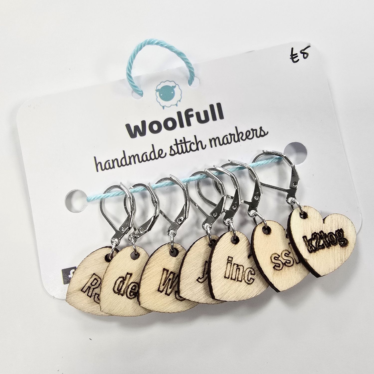 A photo of 7 wooden heart shaped stitch markers with engraved knitting terms on them.