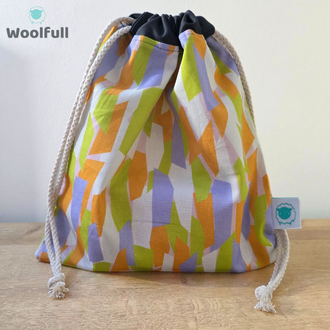 A drawstring bag in a white fabric with green, orange and purple shapes.