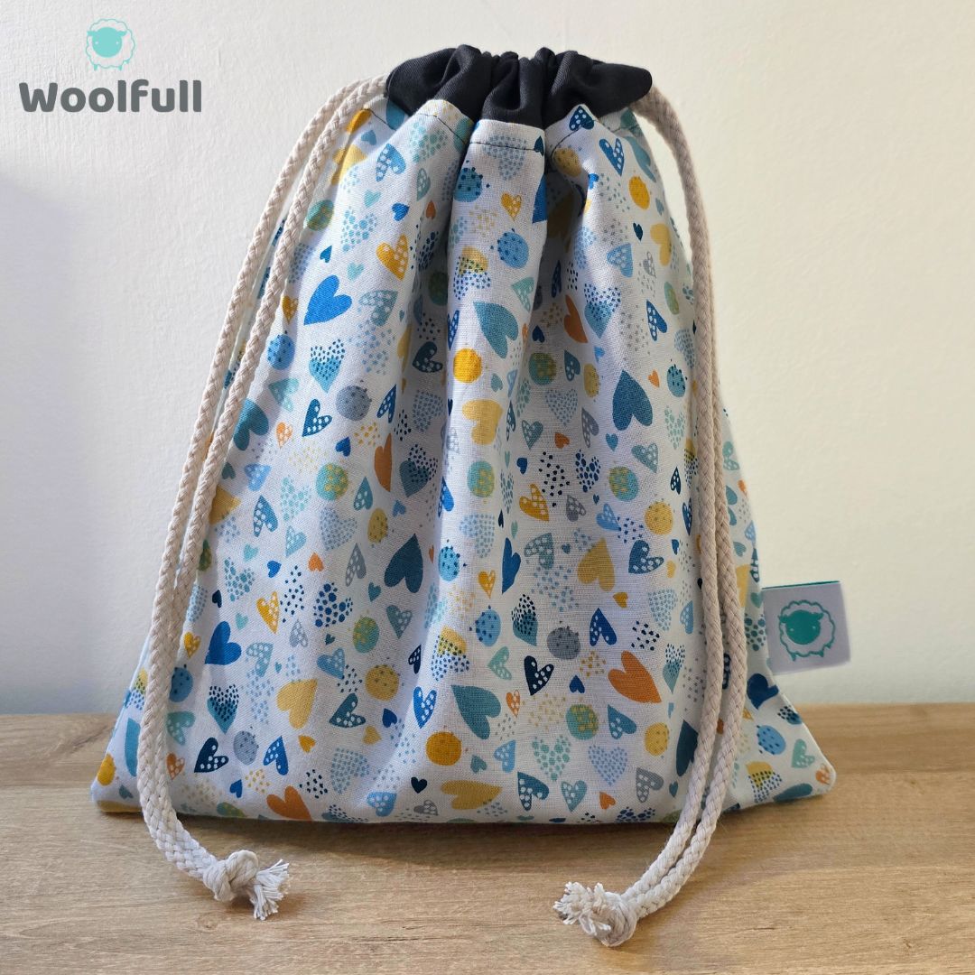 A drawstring bag in a white fabric with blue and orange hearts.