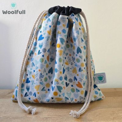 A drawstring bag in a white fabric with blue and orange hearts.