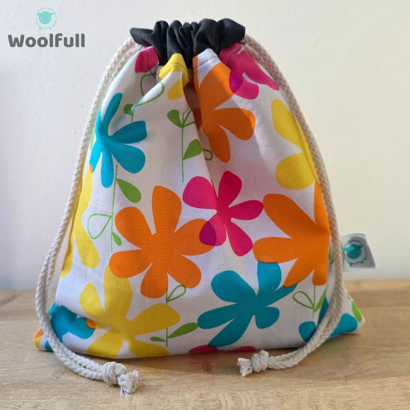 A drawstring bag in a white fabric with bright colourful flowers.