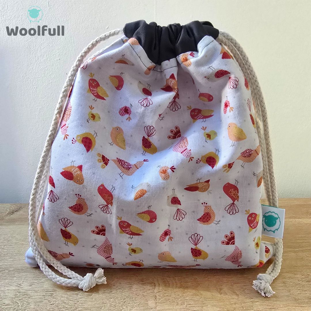 A drawstring bag in a white fabric with red and yellow cartoon birds.